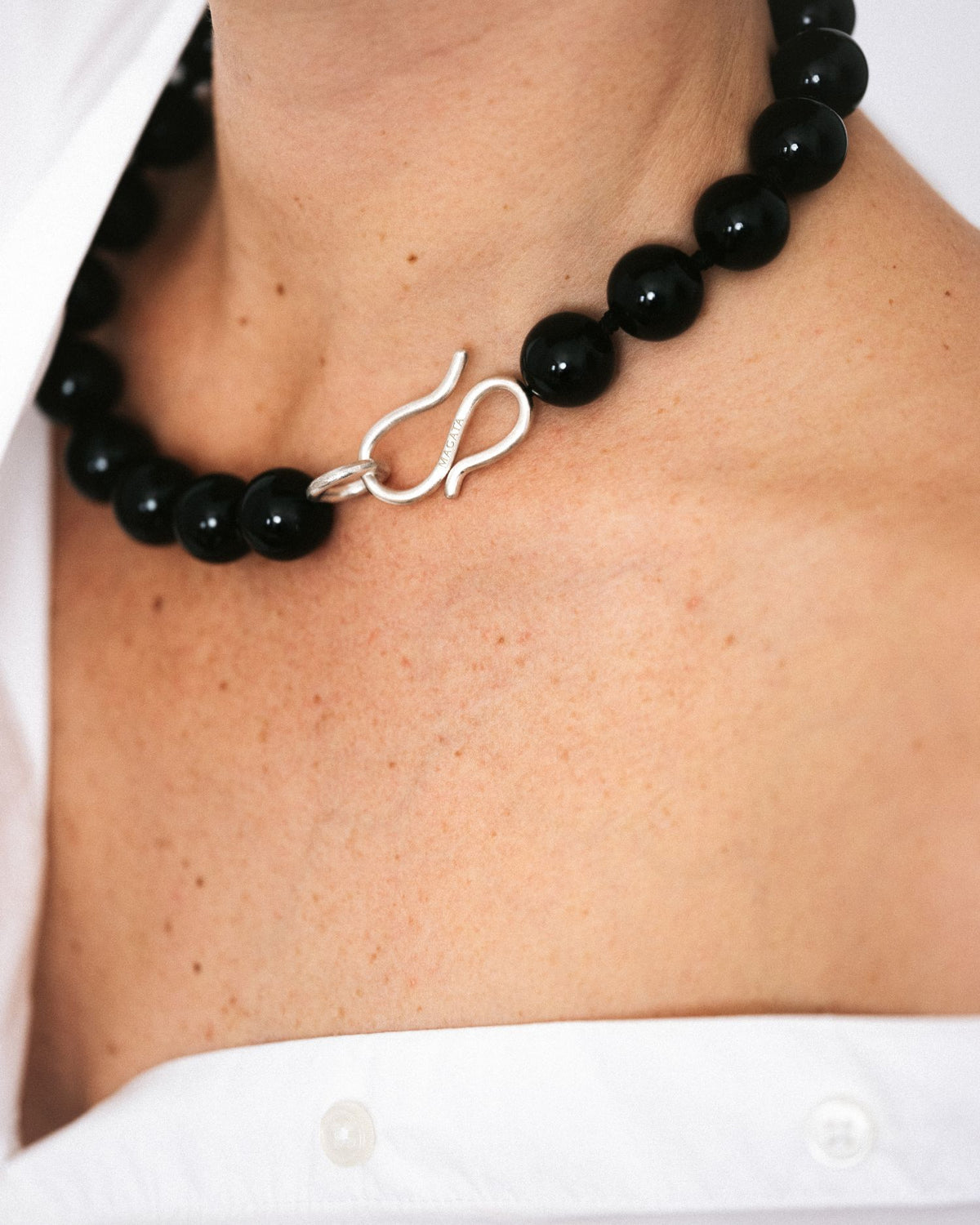 A close-up of a person's neck and chest wearing a black onyx beaded necklace with a polished silver hook clasp