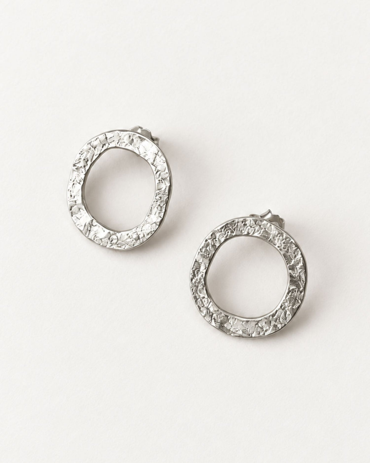 A pair of textured silver hoop earrings with a lunar-like texture, displayed on a clean white background.