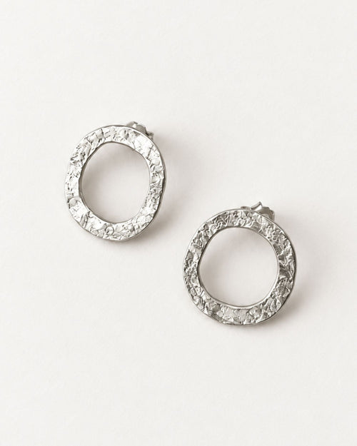 A pair of textured silver hoop earrings with a lunar-like texture, displayed on a clean white background.