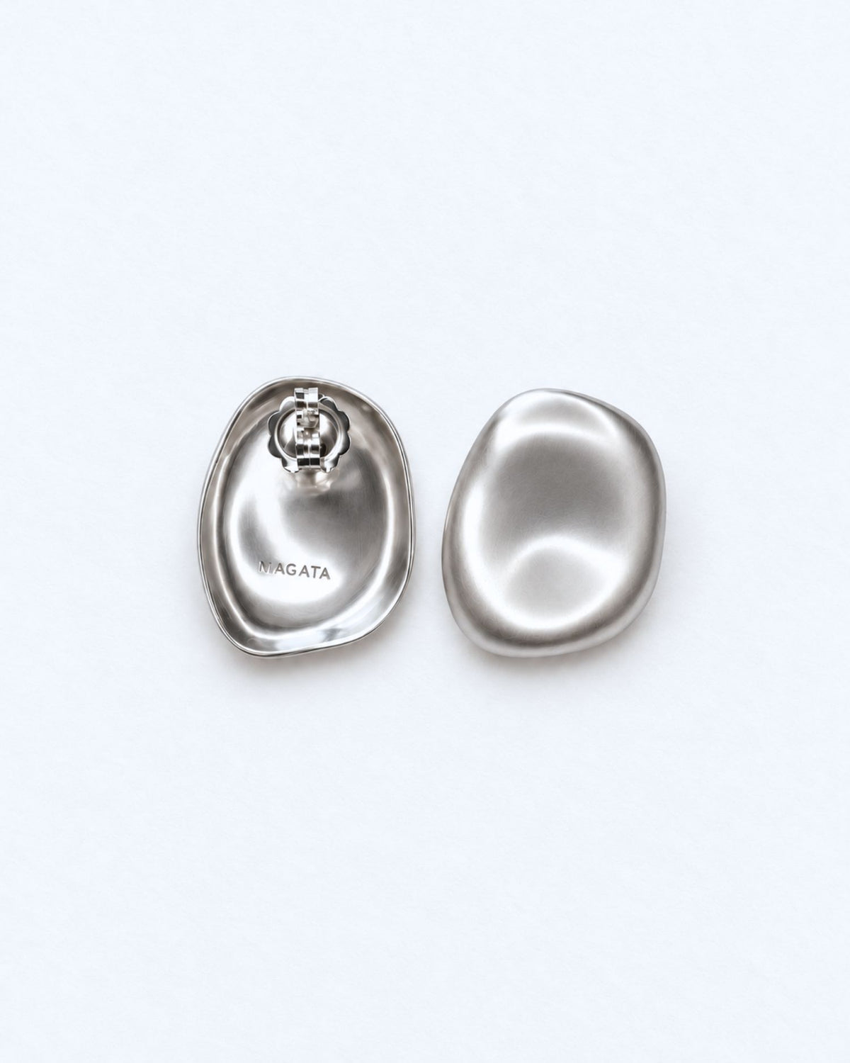 A pair of polished silver earrings shaped like stylised clam shells, shown from both the front and back on a clean white background. The back earring features a visible screw-back clasp and the brand name 'MAGATA' engraved on the inside.