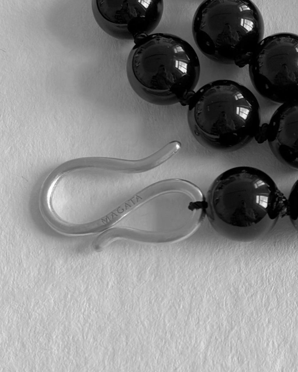 Close up of a Black Onyx beaded necklace with S silver hardware hook on a white textured background