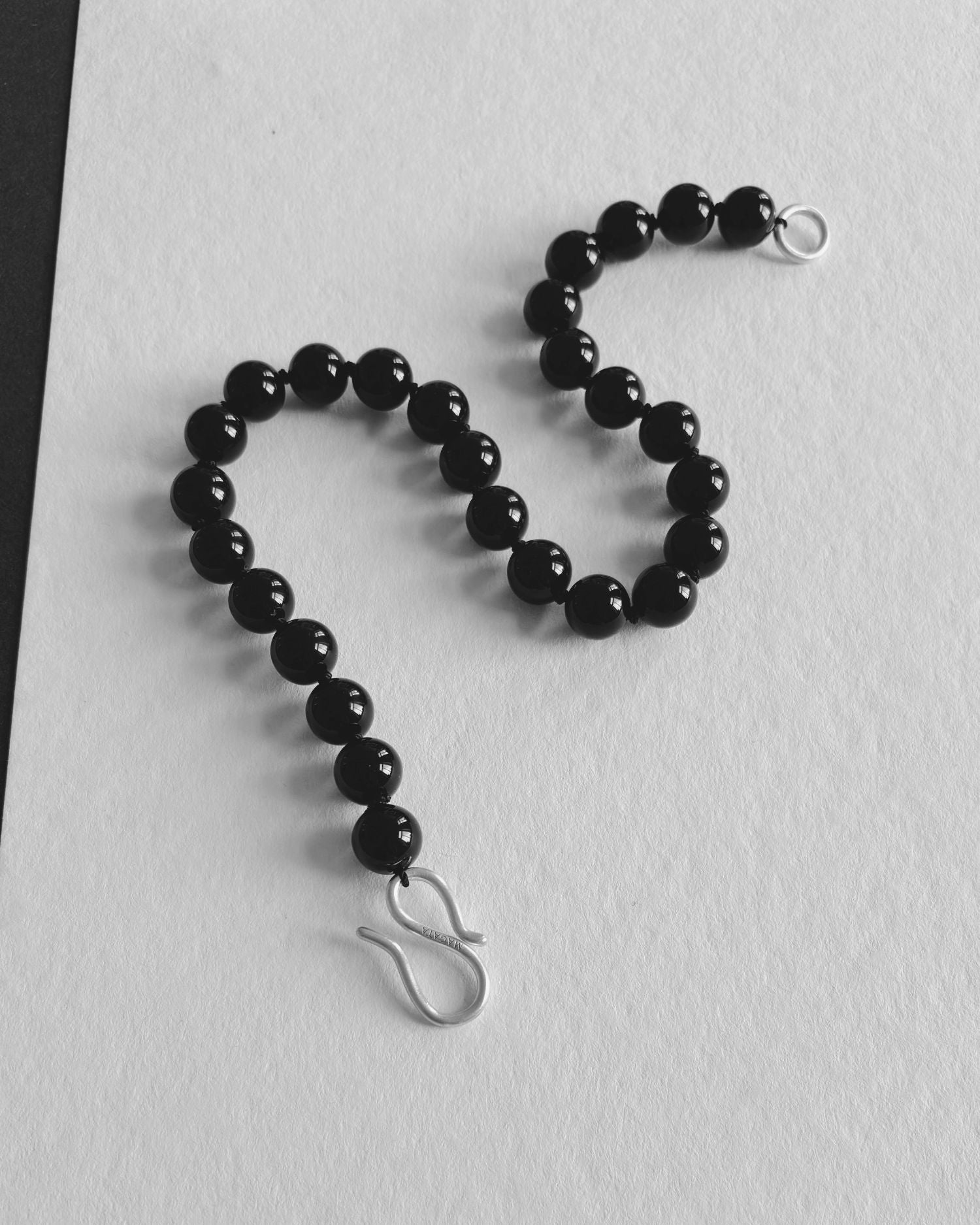 Black Onyx beaded necklace with S silver hardware hook on a white textured background