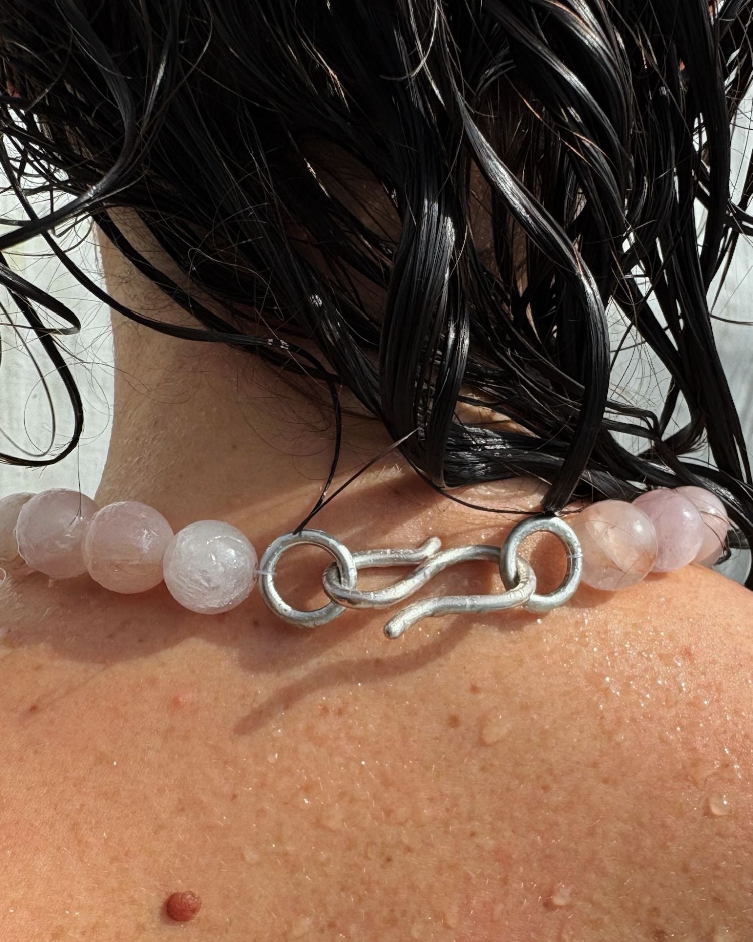 Necklace with pink quartz beads and a silver clasp on a person's neck.