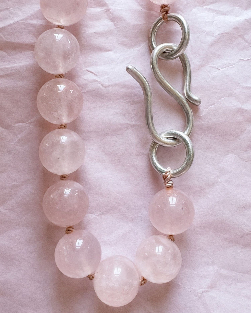 Beaded necklace with pink quartz beads and a silver infinity hook clasp on a pink textured background