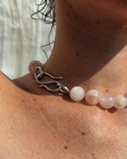 Close-up of a person wearing a beaded necklace with pink quartz beads and silver S hook clasp.