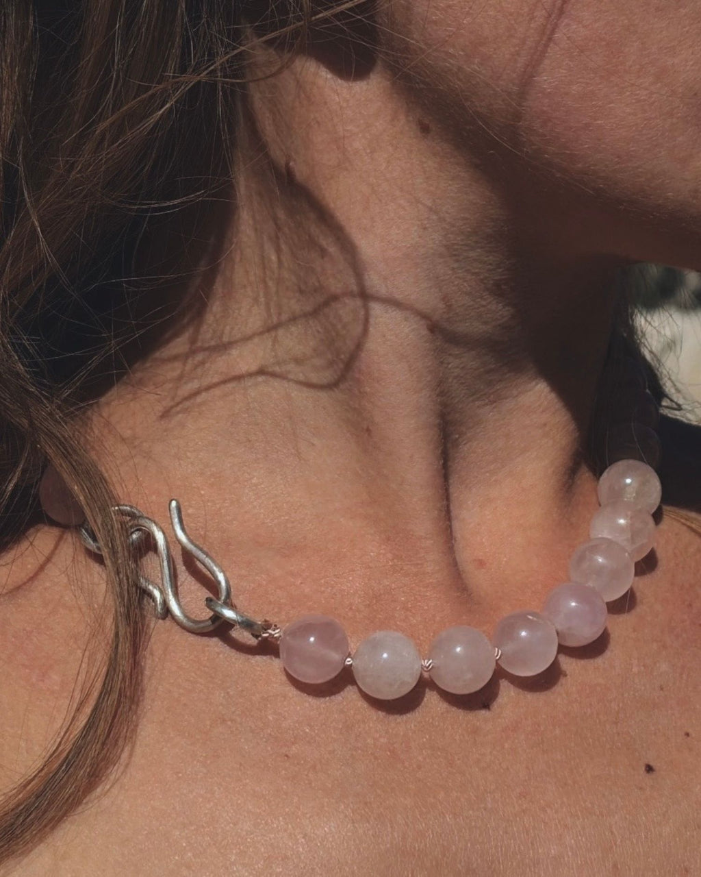 Close-up of a person wearing a beaded pink quartz necklace with a silver infinity hook.