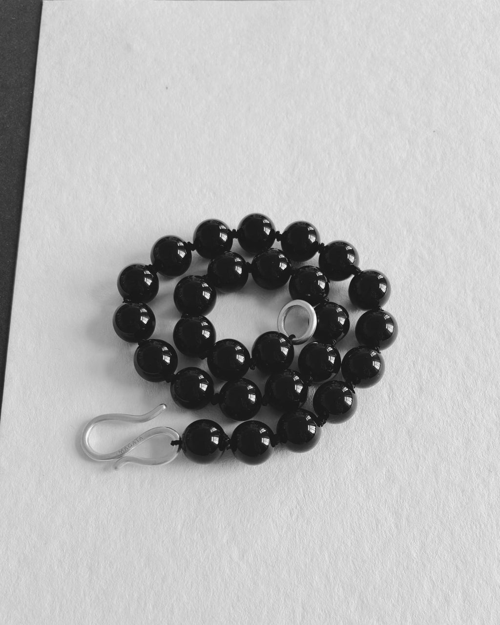 Black Onyx beaded necklace with S silver hardware hook on a white textured background