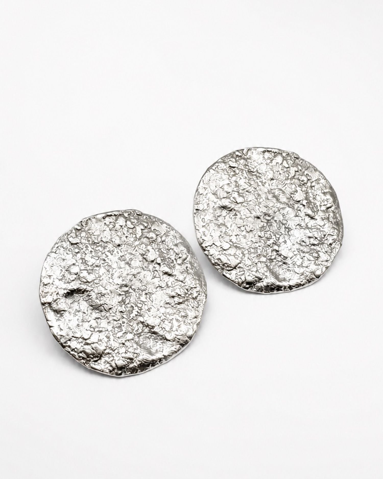 Pair of silver round earrings with moon textured surface on a white background
