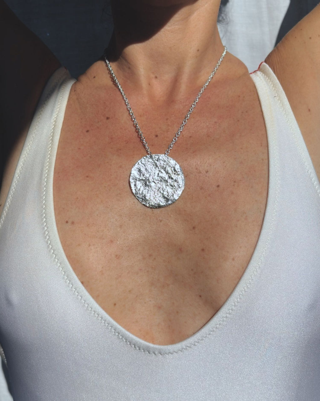 Silver chain necklace with a round moon textured pendant on a person wearing a white tank top.