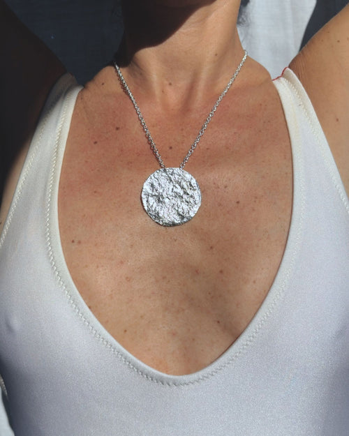 Silver chain necklace with a round moon textured pendant on a person wearing a white tank top.