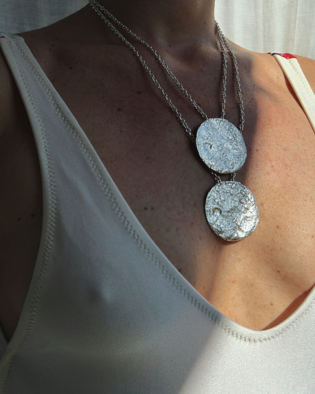 Person wearing a silver rolò chain necklace with two round, moon textured pendants.