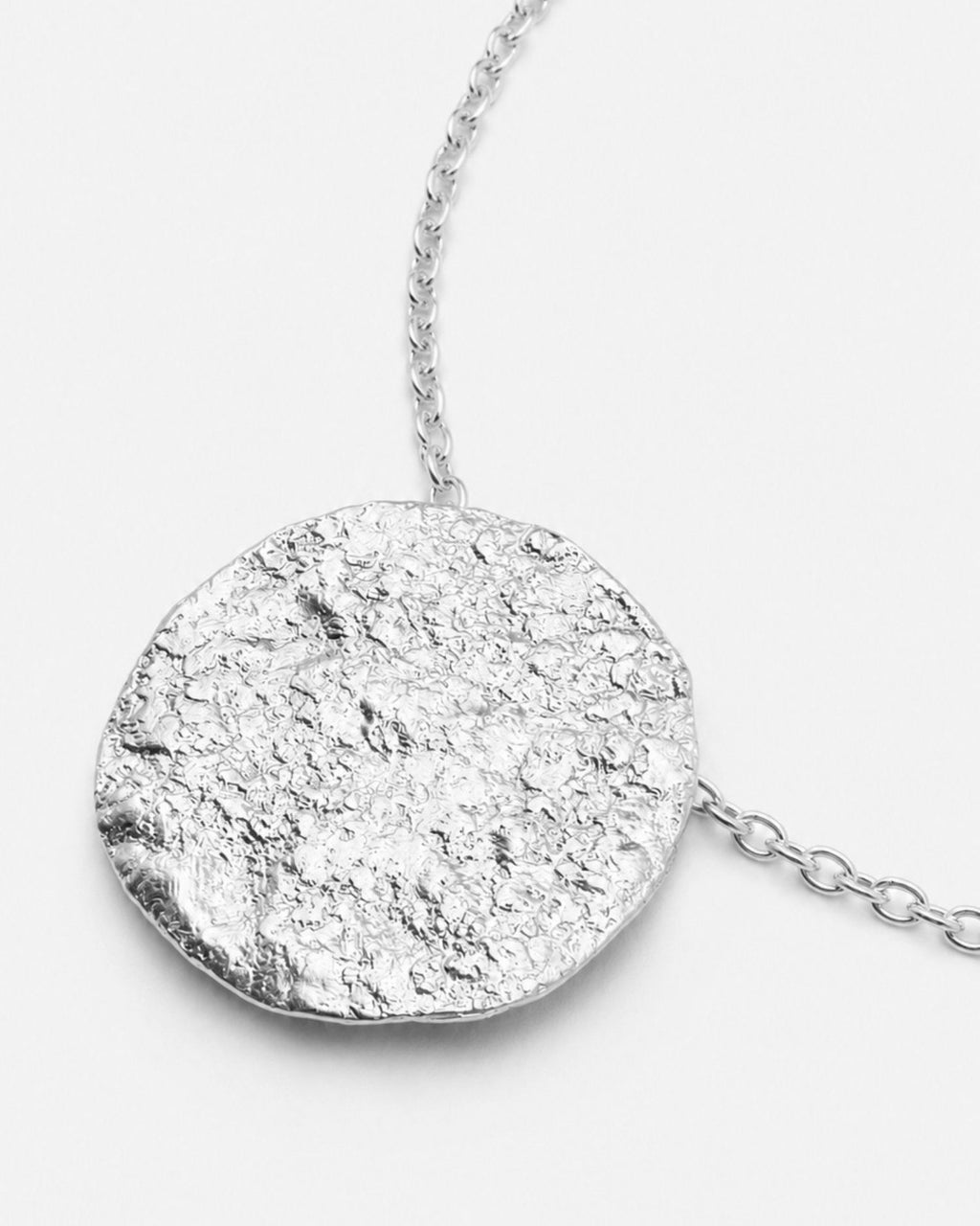Silver chain necklace with a round moon textured pendant on a white background