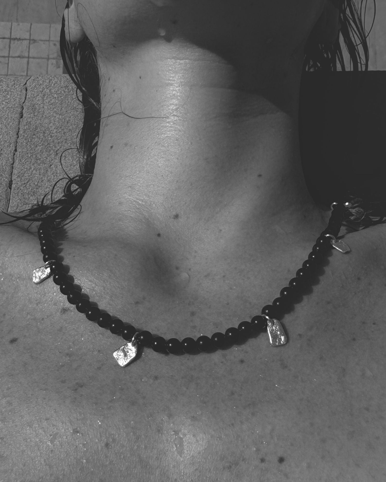 Close-up of a person wearing a black beaded onyx necklace with fragments-shaped pendants.