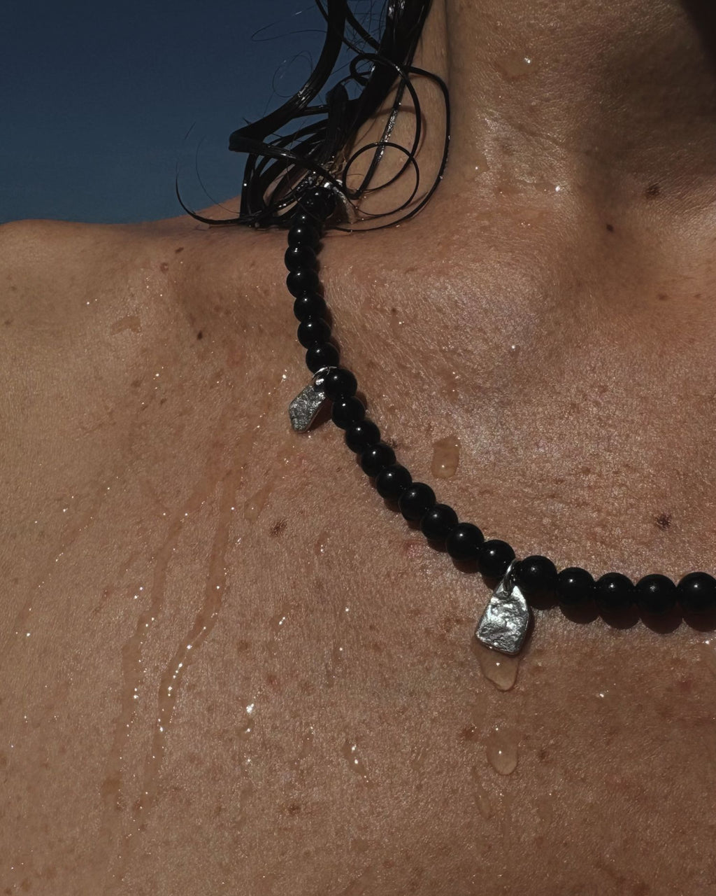 Black onyx beaded necklace with silver pendants on a person's neck against a blue background