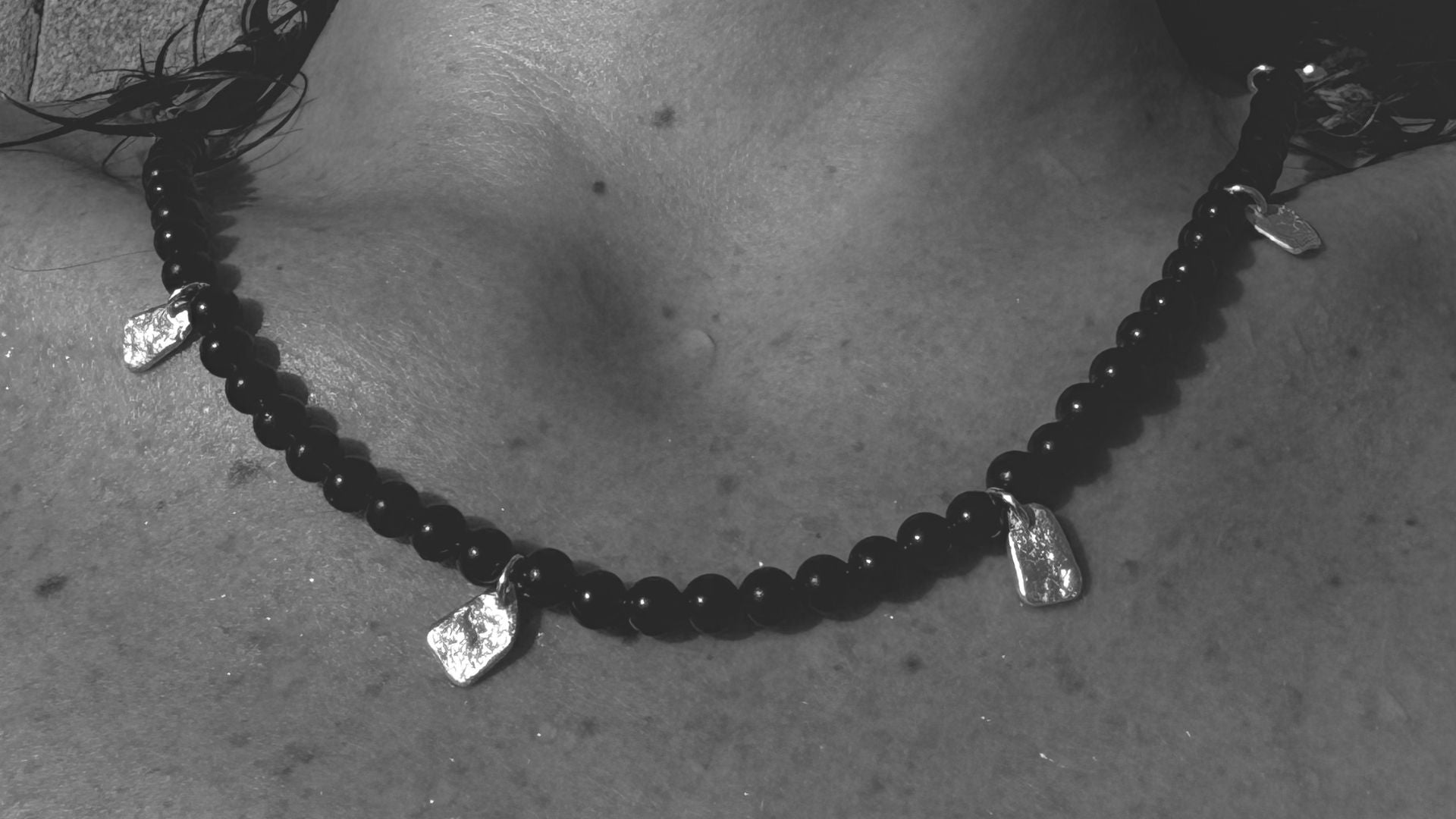 Close-up of a Magata black onyx beaded necklace with silver pendants on wet skin.