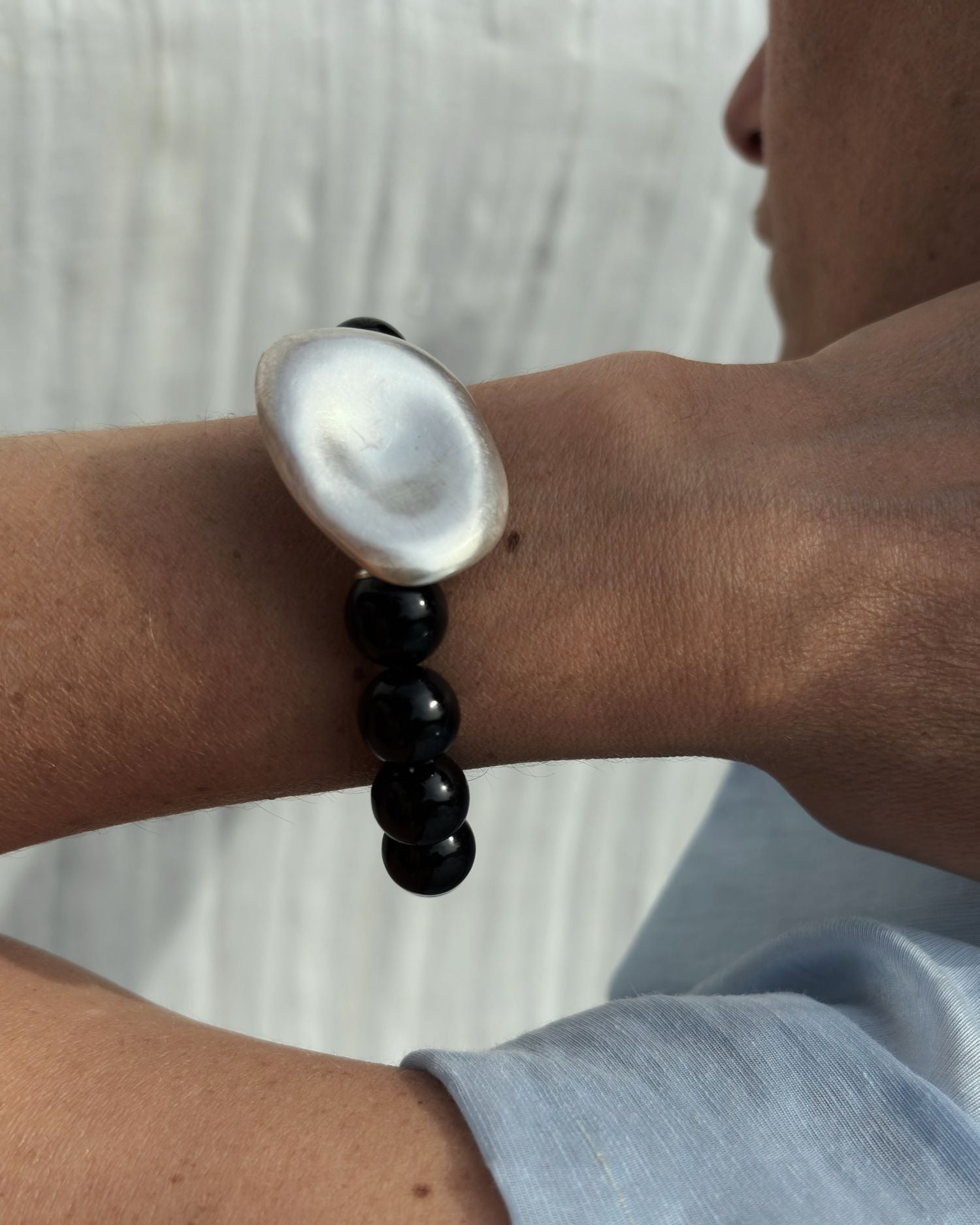 Close-up of a wrist wearing a black onyx beaded bracelet with a tea drop silver clasp and black beads against a neutral background.
