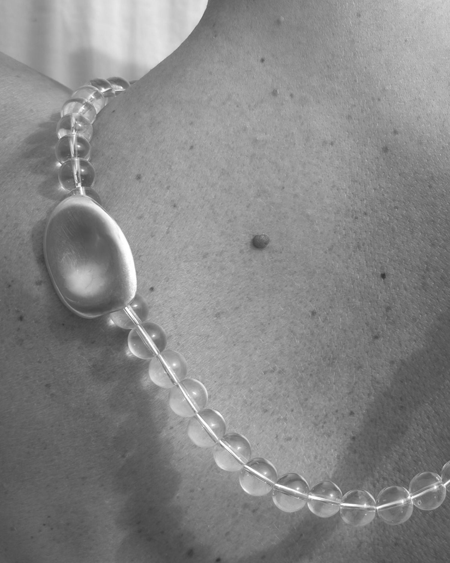 Close-up of a rock crystal beaded necklace with a large pearl pendant on a naked back