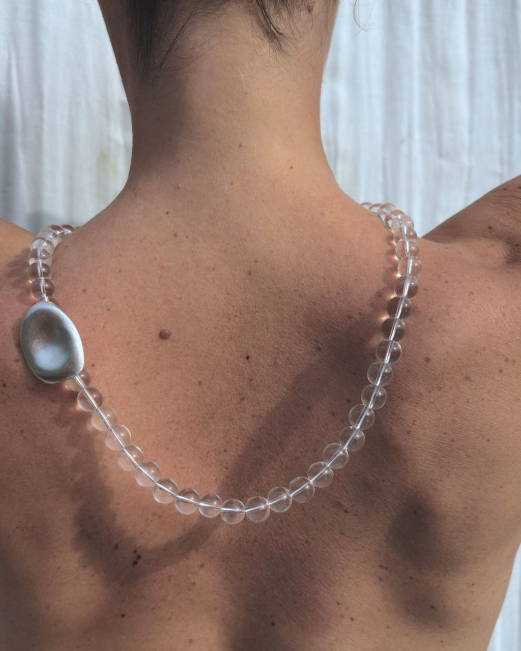 Person wearing a clear beaded necklace with a large silver clasp.