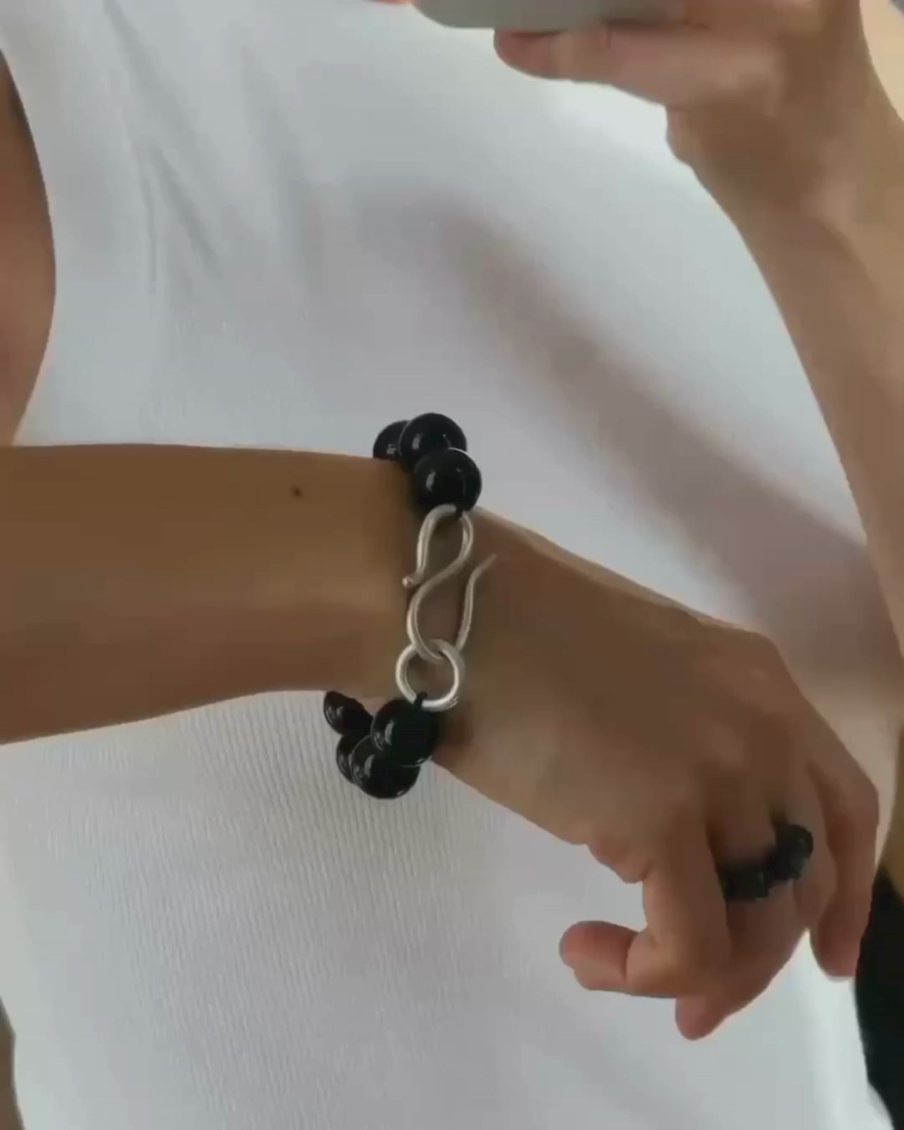 A black beaded bracelet with a polished silver infinity-shaped clasp, displayed moving in front of white top.